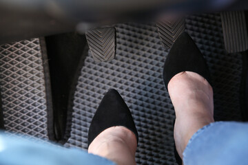 Woman in high heels pushing on pedal of car brake, closeup