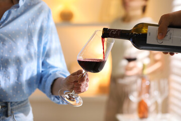 Man pouring red wine into woman`s glass indoors, selective focus
