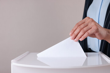 Woman putting her vote into ballot box against grey background, closeup