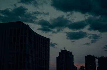 Fototapeta premium Silhouettes of tall multi-story buildings against a dark blue cloudy sky at sunset dusk. View of tall residential houses in a big city in a twilight.