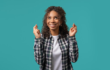 African teenager girl praying crossed fingers on blue. Young adult begs someone