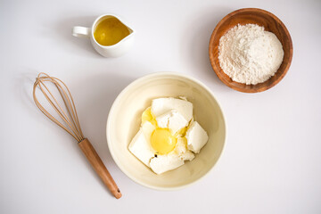 Baking ingredients: flour, egg, whisk, oil and cottage cheese on a white background. Copy space, top view. Baking concept.