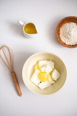 Baking ingredients: flour, egg, whisk, oil and cottage cheese on a white background. Copy space, top view. Baking concept.