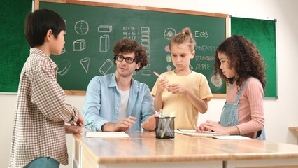 Smart teacher explain idea while diverse children drawing mind map while group of diverse student working together to do class work. Attractive instructor teaching and talking about working. Pedagogy.