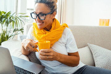 Front view of a happy adult woman working on her laptop during a video call, wearing a yellow...