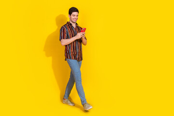 Full length portrait of nice young man walk use phone wear shirt isolated on yellow color background