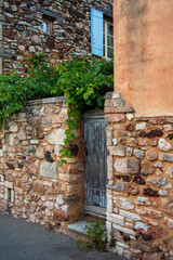 Rustic stone wall with a wooden door and green vines in a village