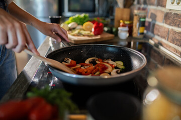 Close-up of a woman cooking vegetables in a pan on the stove