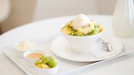 Bowl of fresh fruit with ice cream served on a white tray with kiwi slices, honey, and cream. Delicious and refreshing dessert.