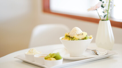 A delicious bowl of dessert with ice cream and fruit slices on a white table in a bright and minimalist setting.