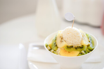 Refreshing bowl of shaved ice topped with kiwi and other fruits on a white background in a bright, clean setting.