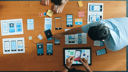 Top view of smart Ui designer brainstorming and planning about Ux Uo design or mobile interface wireframe design with diverse develop team. Caucasian programer walking and joining meeting.Convocation.