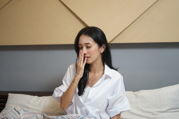 woman waking up in bed yawning and grimacing early morning after sleep sitting in bedroom