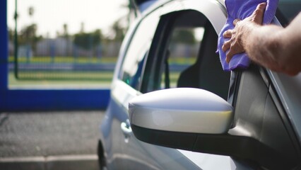 A middle-aged person's hand carefully cleans the side of a silver car. 