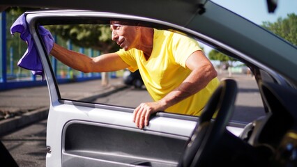 A mature man carefully cleans the interior of a car. The image highlights the care and precision he applies to vehicle maintenance, focusing on the details within the car.