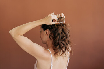 Back view of a redhead woman braiding her hair in a ponytail.