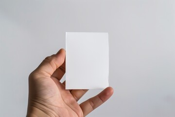 Close-up of a hand holding an empty white post-it note on plain white background, background with copyspace for motivational text, slogan, message