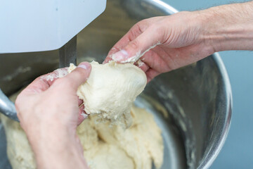 The dough for bread or donuts in the hands of a technologist or baker is checked for readiness and quality against the background of a production planetary mixer. Close-up. Selected focus.