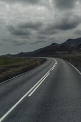 A winding road cuts through Iceland's rugged volcanic landscape under a dramatic sky