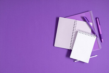 Back to school. Stack of notebooks, open notepad with pen on purple background. Office desk with copy space. Flat lay, top view