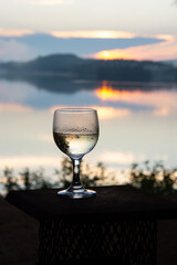 Glass of chilled white wine at sunset by a wild lake.
