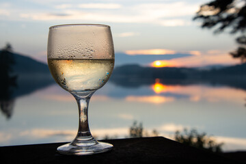 Glass of chilled white wine at sunset by a wild lake.