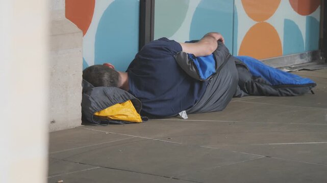 A homeless man sleeping on a street in a sleeping bag.