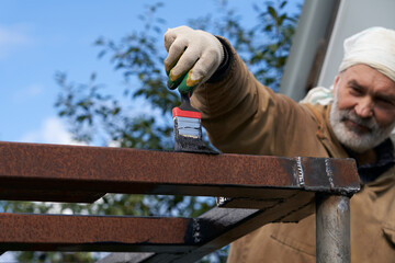 A grown man paints a metal structure with anti-corrosion paint.
