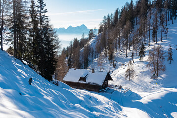 Remote wooden hut on Wertschacher Alm, Bleiberger Eisenerz, Carinthia, Austria. Scenic view of snow capped mountain peak Mangart and Jalovec, Julian Alps. Winter wonderland, Austrian Alps tranquility