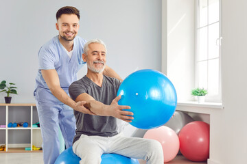 Young male rehabilitation caregiver, nurse helping to disabled aged male patient to exercise with fitness ball, physical therapist teaching, supporting therapy, nursing for aftercare and physiotherapy