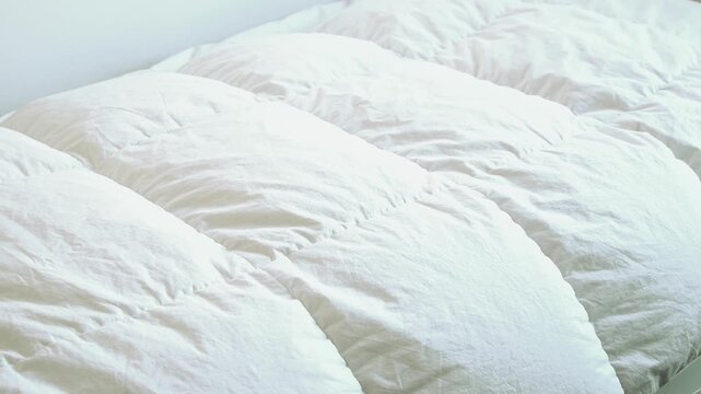 ふわふわの羽毛布団をシングルベッドにかける女性