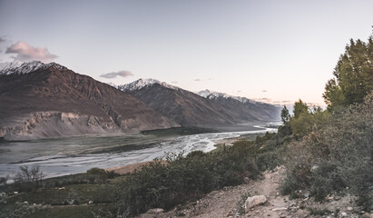 Panorama of the rocky mountain range of the Tien Shan with snow and glaciers and the Wakhan corridor with the Panj River in valley in the evening at sunset in the Pamirs in Tajikistan, for background