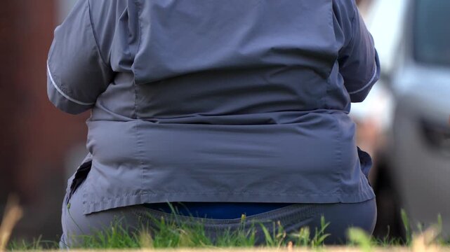 An obese person sat down while people walk past in a town centre
