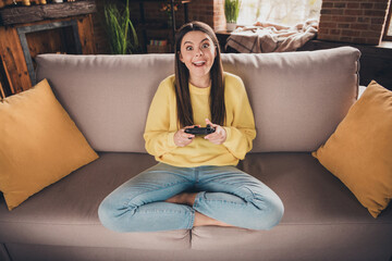 Obraz premium Full length photo of nice teen lady sit sofa excited playstation play video game dressed yellow garment spend pastime spacious indoors room