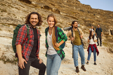 Portrait of a hiking couple surrounded by a group of friends on the the mountains during vacation hike. Atmosphere is palpable as the hiking team forms a community on the mountain backdrop.