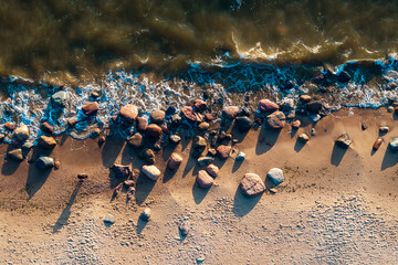 large rocks scattered along the sandy beach with waves crashing over them