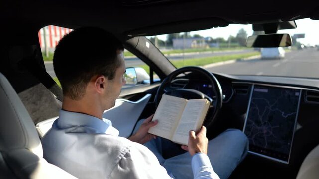 Male businessperson reading book during riding on electrical vehicle with autopilot at urban road. Successful businessman improving his knowledge while riding an autonomous self driving electric car
