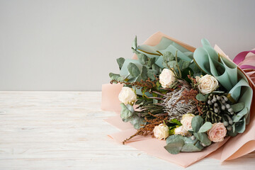 Beautiful bouquet with white roses, protea, brunia branches on a grey background, space for text.