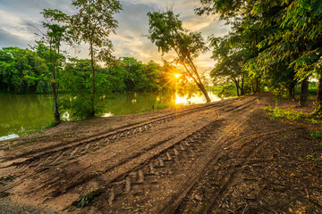 Tire marks on a dirt road in the countryside landscape lake views and the reservoir the forest summer with evening blue dramatic sunset sky nature background.