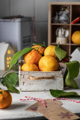 Tangerines (oranges, clementines, citrus fruits) with green leaves in wooden box on kithchen table in cozy Christmas atmosphere. Vertical