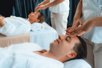 Caucasian couple enjoying relaxing anti-stress head massage and pampering facial beauty skin recreation leisure in dayspa modern light ambient at luxury resort or hotel spa salon. Quiescent