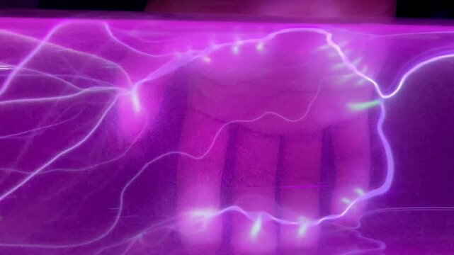 Pink gas discharge in transparent glass tube with man's hand on background