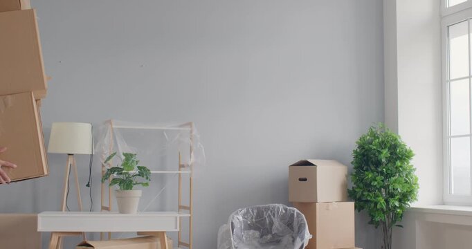 Young man carrying stack of cardboard boxes in hands and falling down on the floor in new apartment while moving into new house. Move, rent and relocation concept. 4k video. slow motion video.
