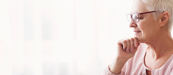 Senior lady with red glasses reading at home, touching her chin, close up, copy space