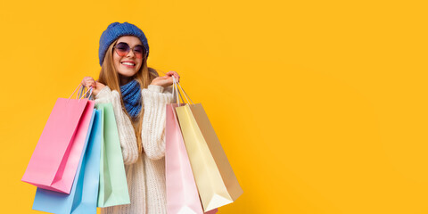 Season of sales. Happy young woman in knitted hat and sunglasses with shopping bags, pink studio...