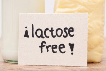 Milk in glassware and a piece of cheese, card with the phrase “Lactose free” on wooden table. Space for text