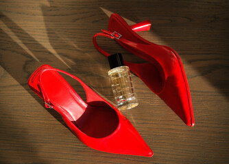 A stylish composition featuring red high-heeled shoes and a glass perfume bottle on a wooden floor, bathed in natural light. The items are arranged elegantly, highlighting luxury and fashion.