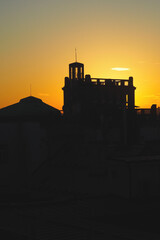 A silhouetted building with a tower against a vibrant orange sunset sky. The image captures the peaceful transition from day to night and contrast between light and shadow. From Lucerna, Prague CZ