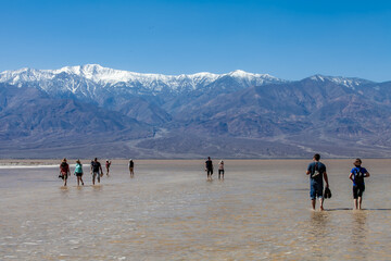 Tourists walking on Lake Manly in Death Valley National Park with snow covered mountains in background after a spring rain