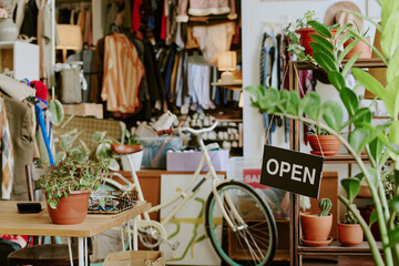 Cozy retail space featuring various potted green plants and an open sign, creating inviting atmosphere with bicycles and shelves adding to the charm